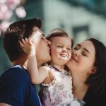 Happy young parents with a little daughter stand under blooming pink tree outside