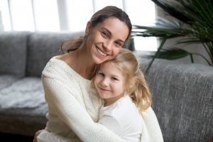 Portrait of happy loving single mother hugging cute little daughter, smiling young woman embracing preschool kid girl, diverse mom and adopted child looking at camera, sincere warm family relations