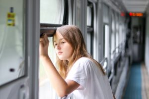 Beautifull pensive preteen girl looking sadly at the window in the compartment carriage in train sad to leave. Parting and leaving home concept.