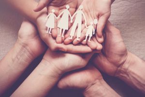 Adult and children hands holding paper family cutout, family home, foster care, homeless support concept