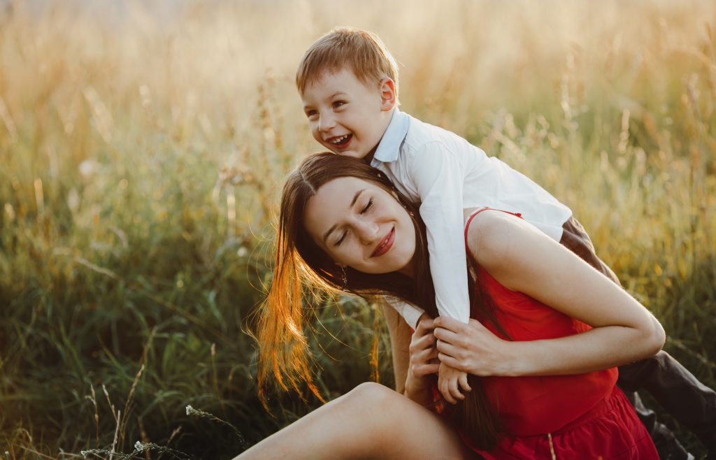 Family portrait, nature. Charming mom and son play on the lawn before the sunset