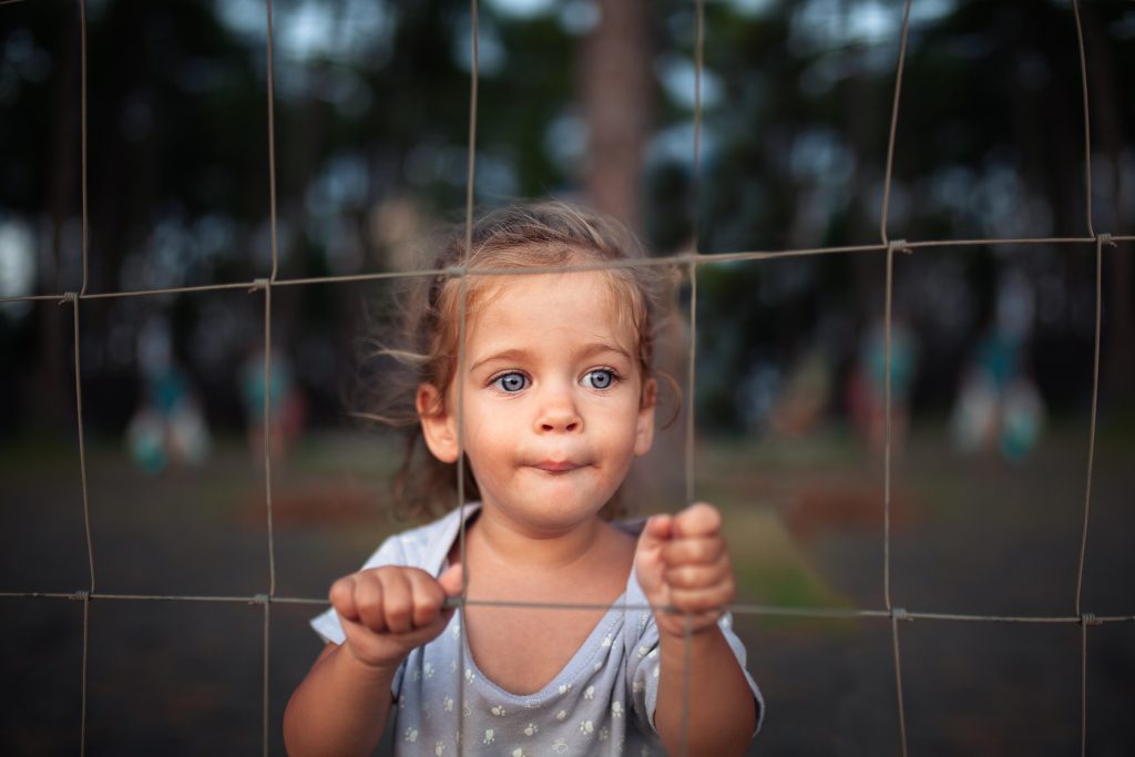 little girl standing against a fence in a park